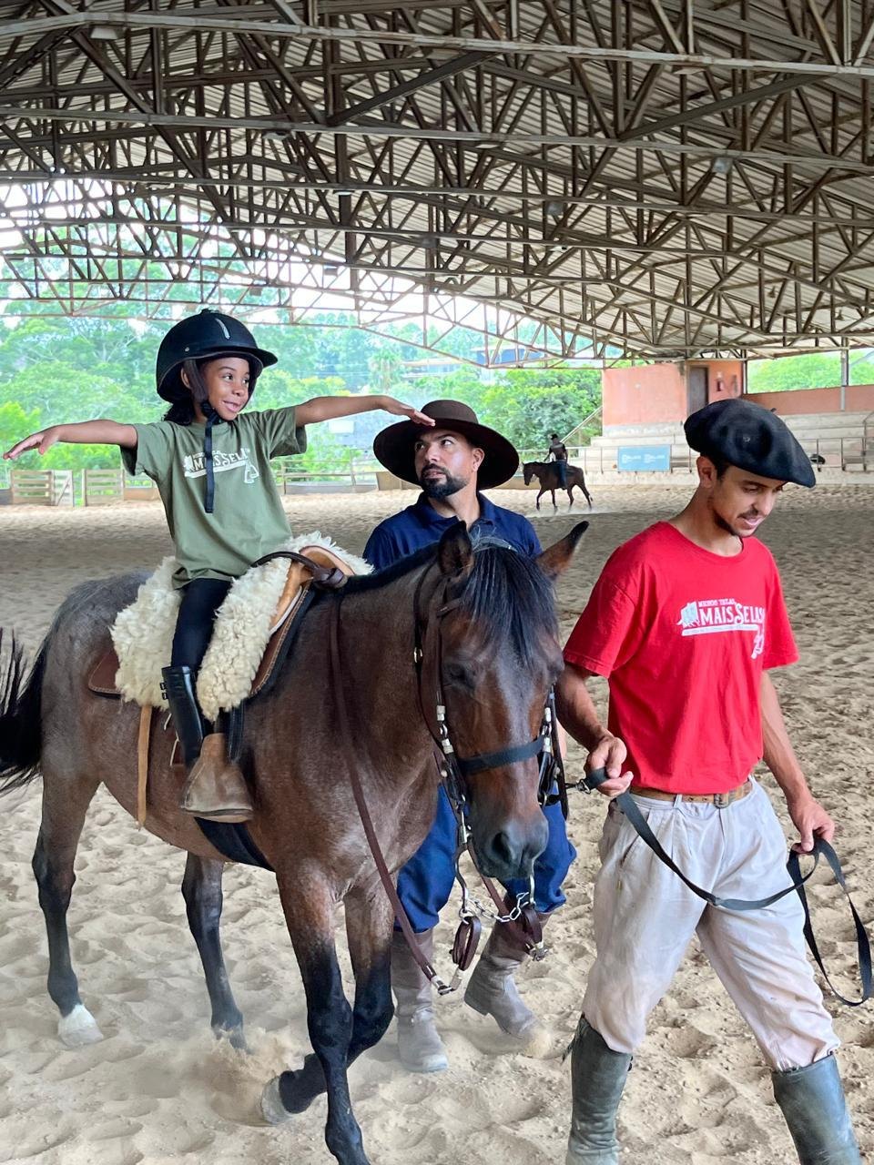 Criança montando a cavalo acompanhada de instrutores